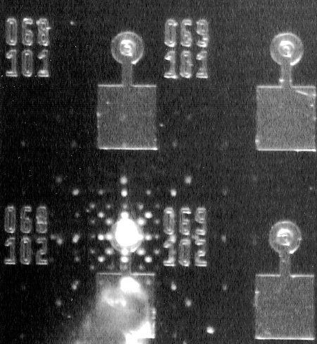 The figure shows several VCSELs still on wafer after processing, with one of them under operation. The contact structures, and in the center of their circular part, the active part of the lasers with a diameter of about 5 µm can be seen.