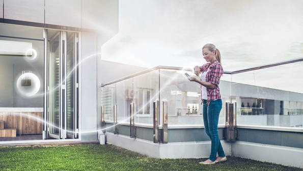 Woman with tablet in hand standing on a roof top terrace and is connected to her smart home