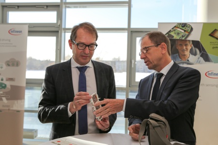 Der Vorstandsvorsitzende von Infineon Dr. Reinhard Ploss (rechts) erläutert dem Bundesminister für Verkehr und digitale Infrastruktur Alexander Dobrindt einen Leistungshalbleiter für die Motorsteuerung in Elektrofahrzeugen.